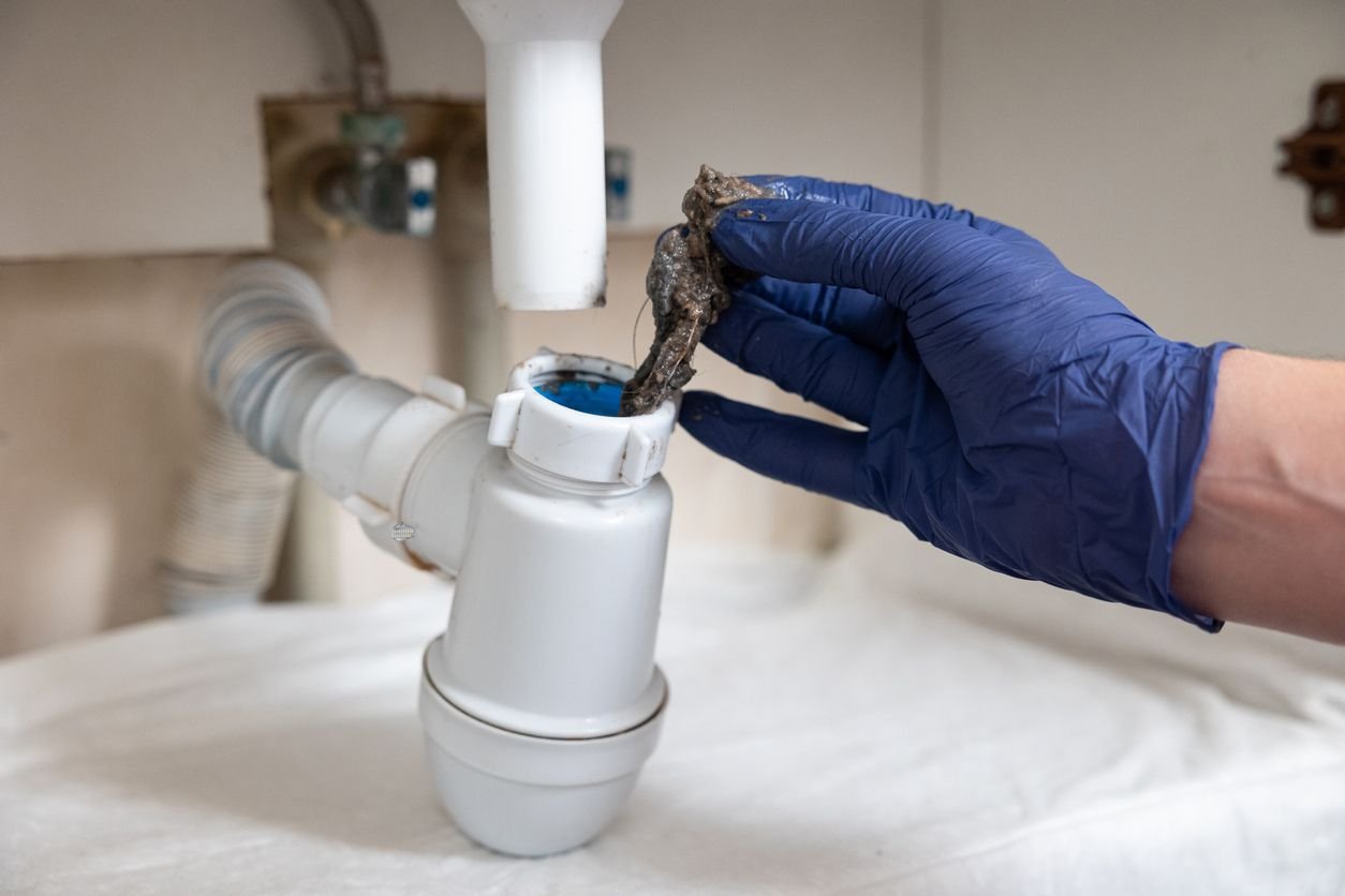 Gloved hand clearing a blockage from a sink trap