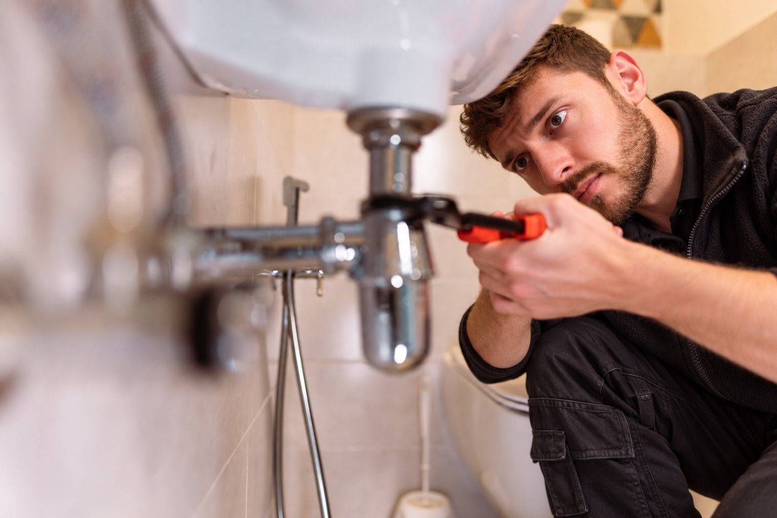 Fast Fix plumber tightening the waste pipe under a bathroom basin