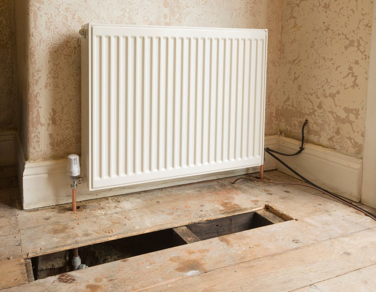 Radiator on a wall above lifted floorboards